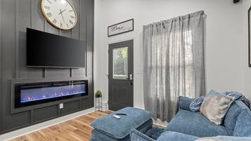 A modern living room with a flat-screen TV, a fireplace, grey walls, a grey sofa, and a door with a window.