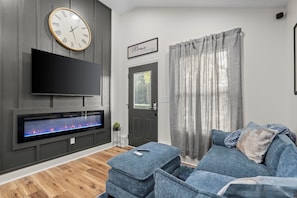 A modern living room with a flat-screen TV, a fireplace, grey walls, a grey sofa, and a door with a window.