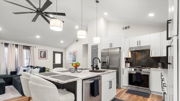 Une cuisine moderne avec des meubles blancs, un îlot central, des appareils en acier inoxydable et des luminaires suspendus.