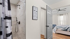 A modern bathroom with a shower, a toilet, and a sink. There is a framed sign on the wall with bathroom-related words.