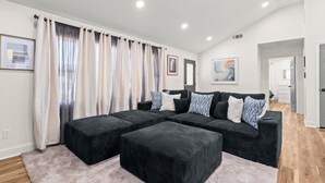A modern living room with a sectional sofa, ottomans, and a large window with curtains.