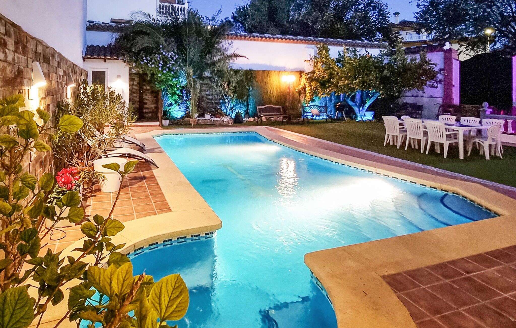 A swimming pool with a tiled deck, surrounded by outdoor furniture and plants.
