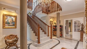 Un magnifique escalier orné de balustrades travaillées, un lustre et un sol en marbre.