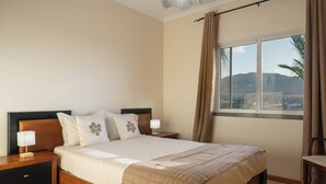 Une chambre avec un grand lit, deux tables de chevet avec des lampes, une fenêtre avec des rideaux et une vue sur l’extérieur.