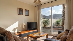 Un salon comprenant un canapé, une table basse, un téléviseur et une porte-fenêtre coulissante donnant sur un balcon avec vue sur le paysage.