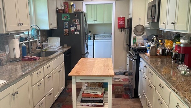 Een keuken met witte kastjes, een houten aanrecht, een centraal eiland met boeken, en een magnetron boven het fornuis.