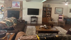 Een woonkamer met een open haard, een aan de muur bevestigde televisie, een boekenkast, een salontafel met decoratieve objecten, en een plafondventilator.