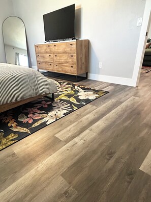 A bedroom with a bed, a wooden dresser, a flat-screen TV mounted above the dresser, and a floral area rug. - Spacious 4-Bed Retreat with Pool Short Stroll to the Beach (Fort Myers Beach)