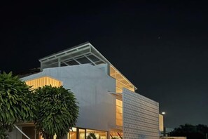 Un edificio moderno con techo inclinado, grandes ventanales y luz interior visible.