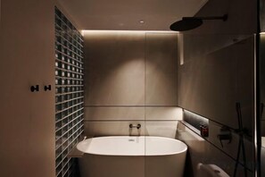 Un baño moderno con una bañera redonda, una cabina de ducha con mampara de vidrio y un estante empotrado con botellas.