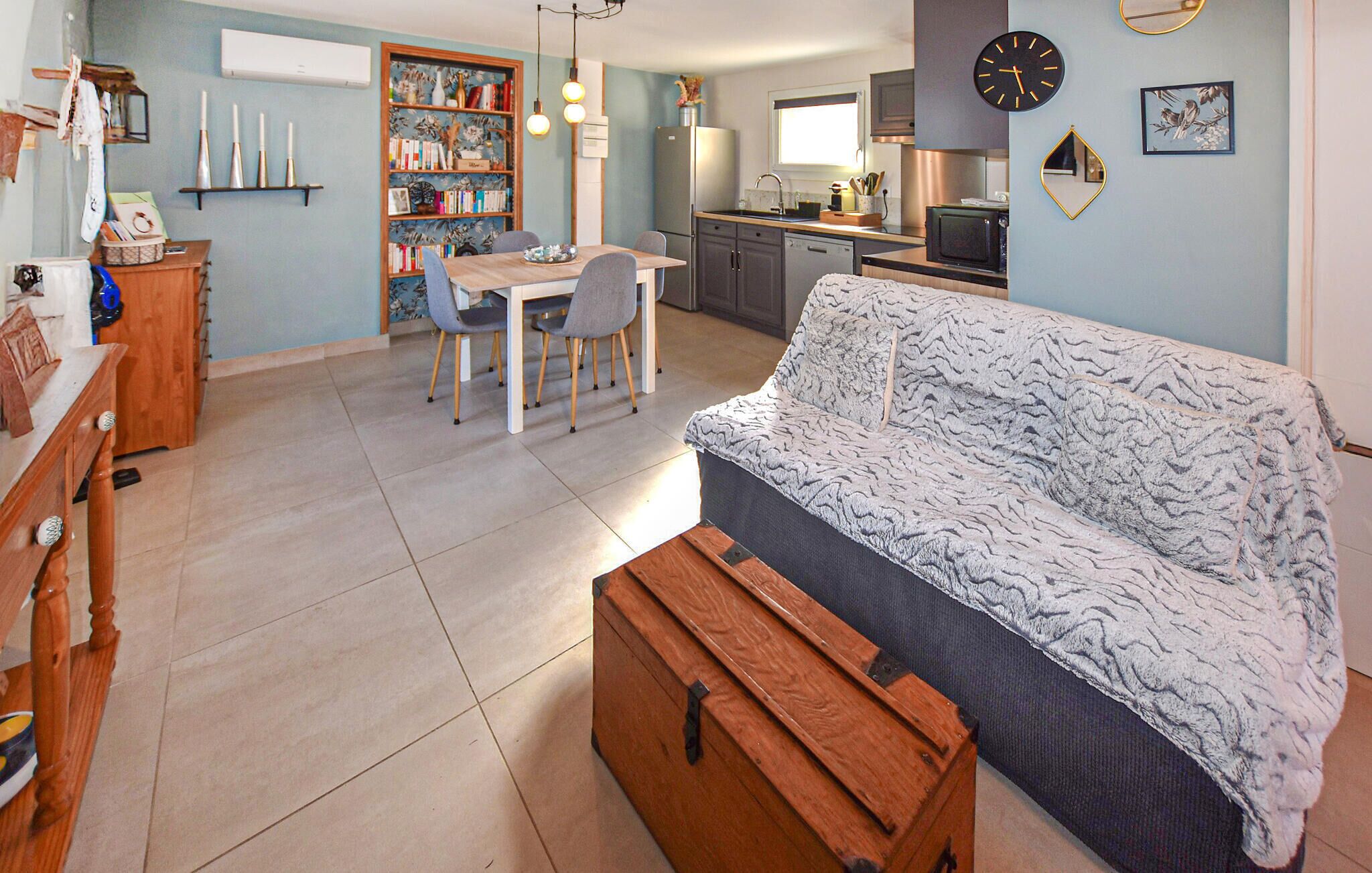 Un espacio habitable compacto con sofá, una mesa de comedor con sillas, una zona de cocina con electrodomésticos modernos y una estantería.