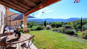 Eine Terrasse mit Tisch und Stühlen, einer hängenden Leuchte und Blick auf eine gebirgige Landschaft.