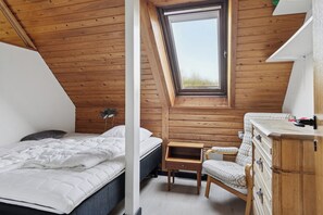 Une chambre avec un plafond en pente, un puits de lumiĂšre, un lit, une table de chevet, une chaise et une commode en bois.