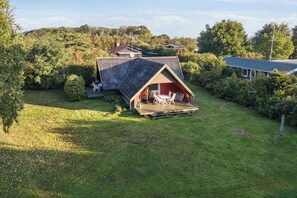 Une maison avec un toit en pente, une terrasse et un espace patio aménagé avec du mobilier d’extérieur.