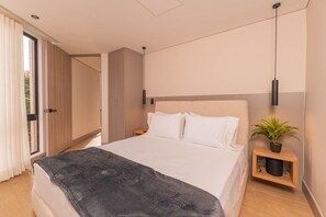 A modern bedroom with a large bed, a bedside table with a plant, and a sliding door leading to an outdoor area.
