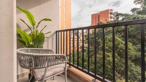 A balcony with a wicker chair, a potted plant, and a view of surrounding buildings and greenery. - 2BR-2AC Apartment in Laureles w/ private balcony (Medellín)