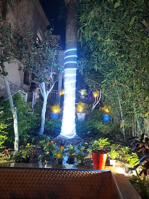 A well-lit outdoor area with a tall, illuminated column, surrounded by potted plants and trees. - Peaceful Villa Retreat Near the Sea and City Center (Tanger)