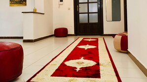 Un corridoio con un lampadario, un tappeto rosso e bianco, una porta in legno e uno specchio a muro.