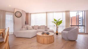 Una sala de estar moderna con un sofá modular, una mesa de centro redonda, un sillón gris y un amplio ventanal con cortinas.