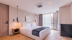 Una habitación de hotel moderna con una cama grande, una mesita de noche, un armario y un ventanal con cortinas.