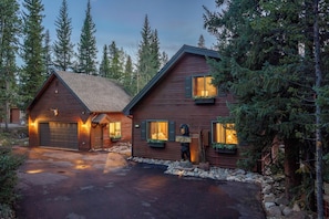 A two-story log cabin with a garage, a welcome sign, and a bear statue.