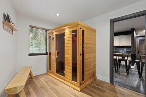 Een kamer met een houten kast, een bank, een raam met zonwering en een open keuken.