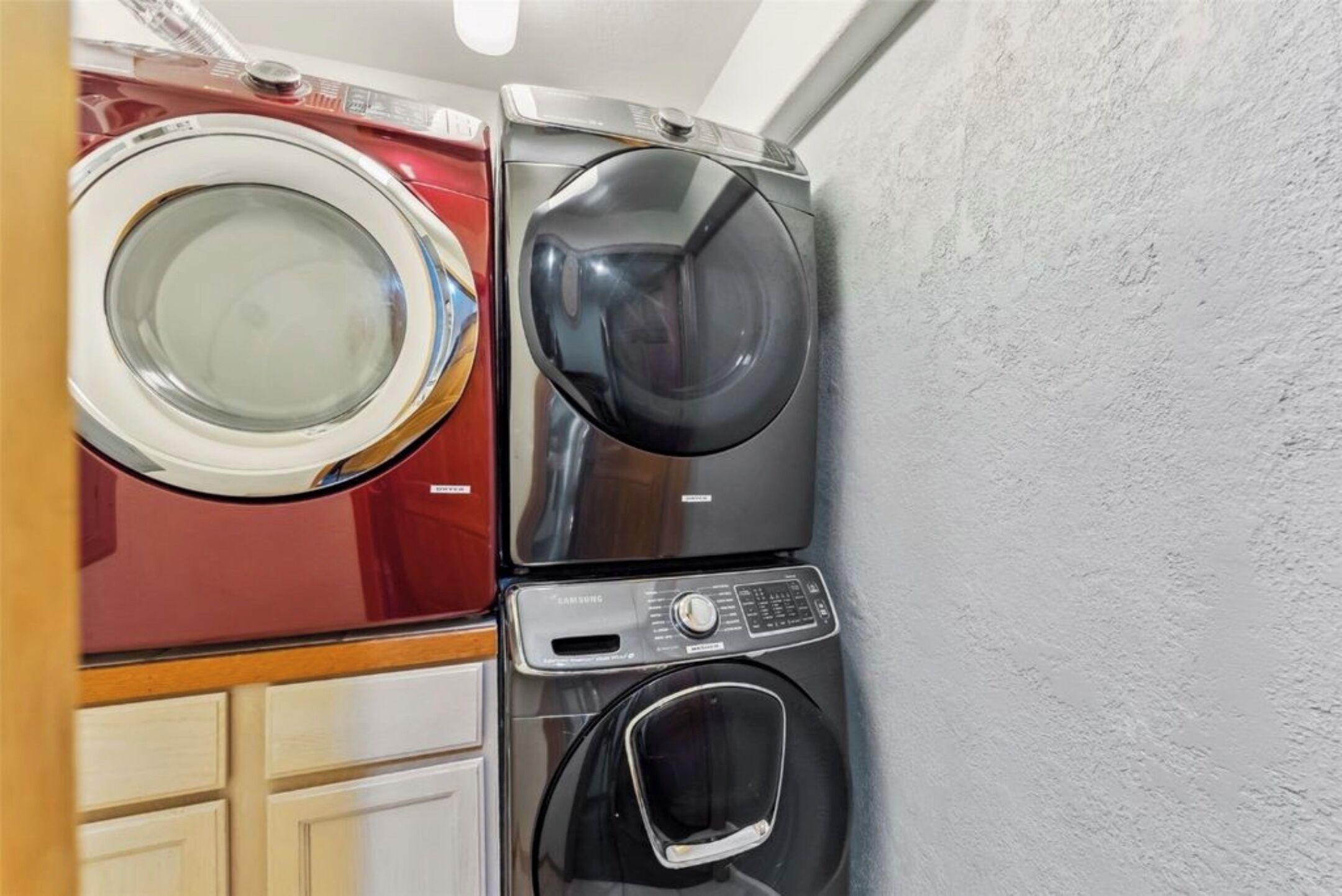 A stacked washer and dryer unit in a laundry room with a wooden cabinet below.