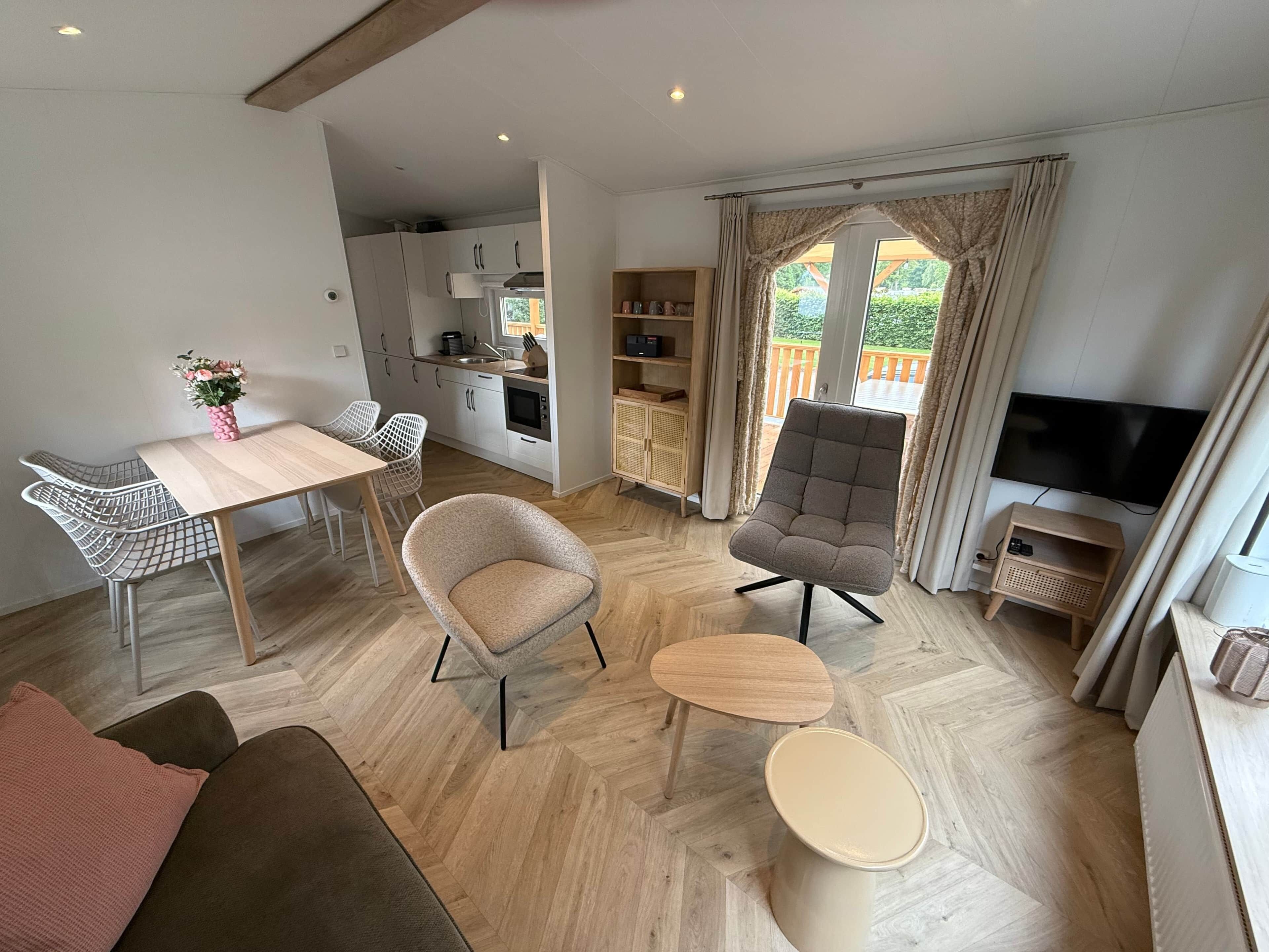A modern living room with a sofa, a dining table with chairs, a grey armchair, a small round table, and a TV.