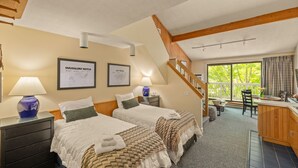 Een hotelkamer met twee bedden, een bureau, een trap en een balkon met uitzicht op bomen.
