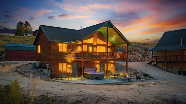 A two-story log cabin with a balcony, a hot tub, and a covered patio area.