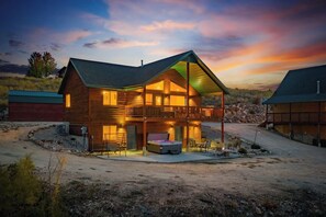 A two-story log cabin with a balcony, a hot tub, and a covered patio area.