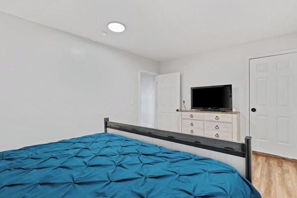 A bedroom with a bed, a television on a dresser, and a door.
