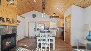 A spacious living area with a fireplace, wooden ceiling, and a dining table with chairs.
