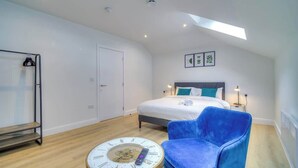A modern bedroom with a bed, a blue chair, a round table with a clock, and a skylight. - Penthouse Flat Manchester. 10 minutes to Airport. Sleeps 8. (Wythenshawe)