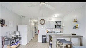A modern kitchen with white cabinets, a dining table, and a ceiling fan. - Beachside Escape (Corpus Christi)