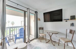 A room with a sliding glass door leading to a balcony, a flat-screen TV mounted on the wall, and a small table with chairs. - Beachside Escape (Corpus Christi)