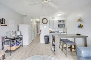 A modern kitchen with white cabinets, a dining table, and a ceiling fan. - Beachside Escape (Corpus Christi)
