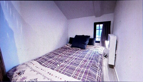 A small, narrow room with a single bed, a window, and a wall-mounted radiator.