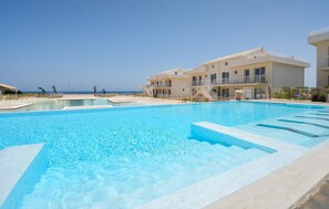 En swimmingpool med krystalklart, blåt vand, omgivet af en hvid bygning med altaner, og en klar himmel.