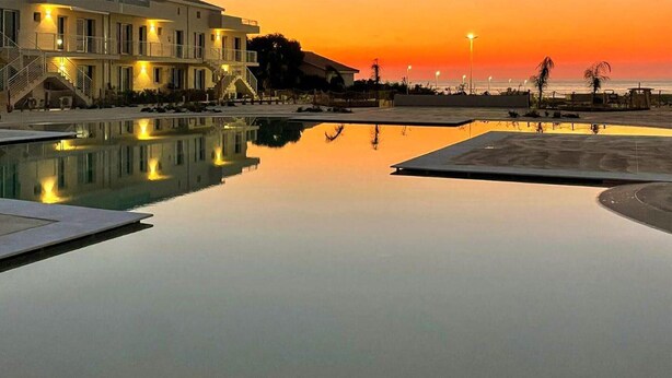 A hotel with a pool reflecting the sunset, a beach, and a staircase leading to the upper floors. - Amazing apartment in Marzamemi with WiFi (Marzamemi)