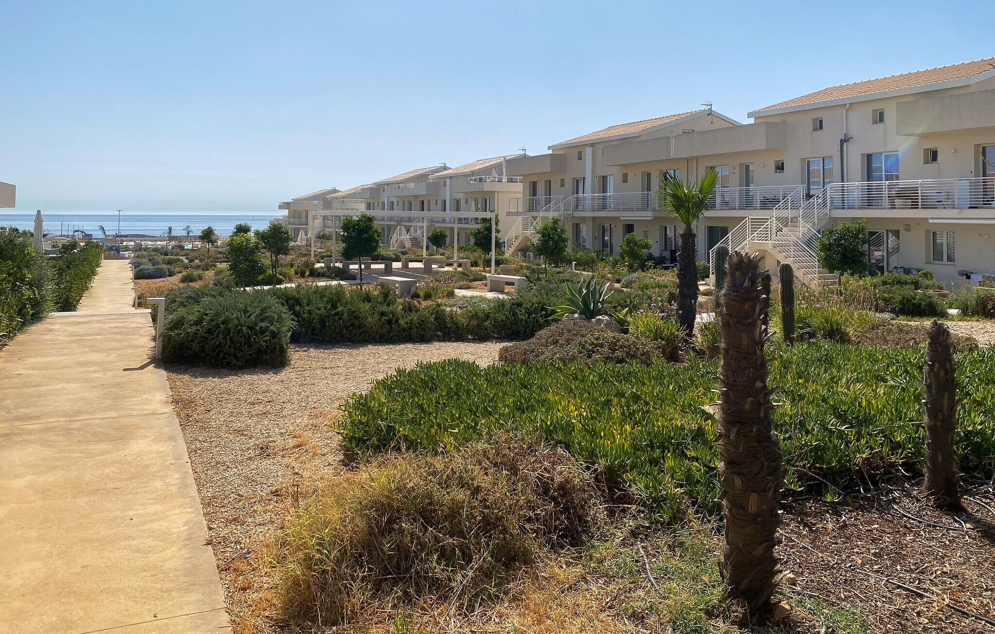 A resort with multiple-story buildings, a paved walkway, and landscaped gardens with cacti and shrubs.