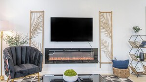 A living room with a flat-screen TV mounted above a fireplace, a dark armchair, and a modern coffee table with a decorative bowl. - Family-Friendly 10 Beds Stay NOLA (New Orleans)