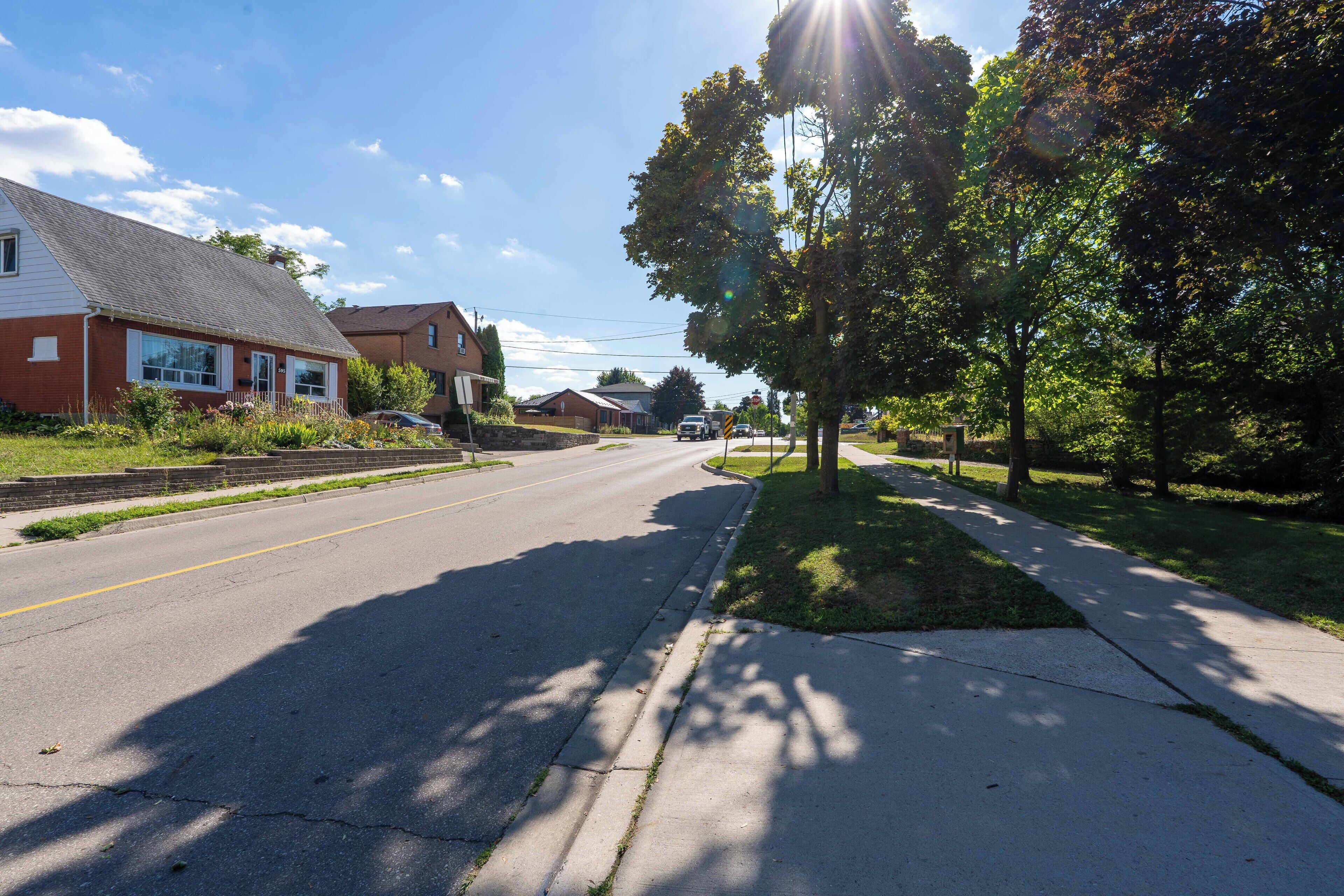 Une rue résidentielle bordée de maisons, avec un trottoir et des arbres.