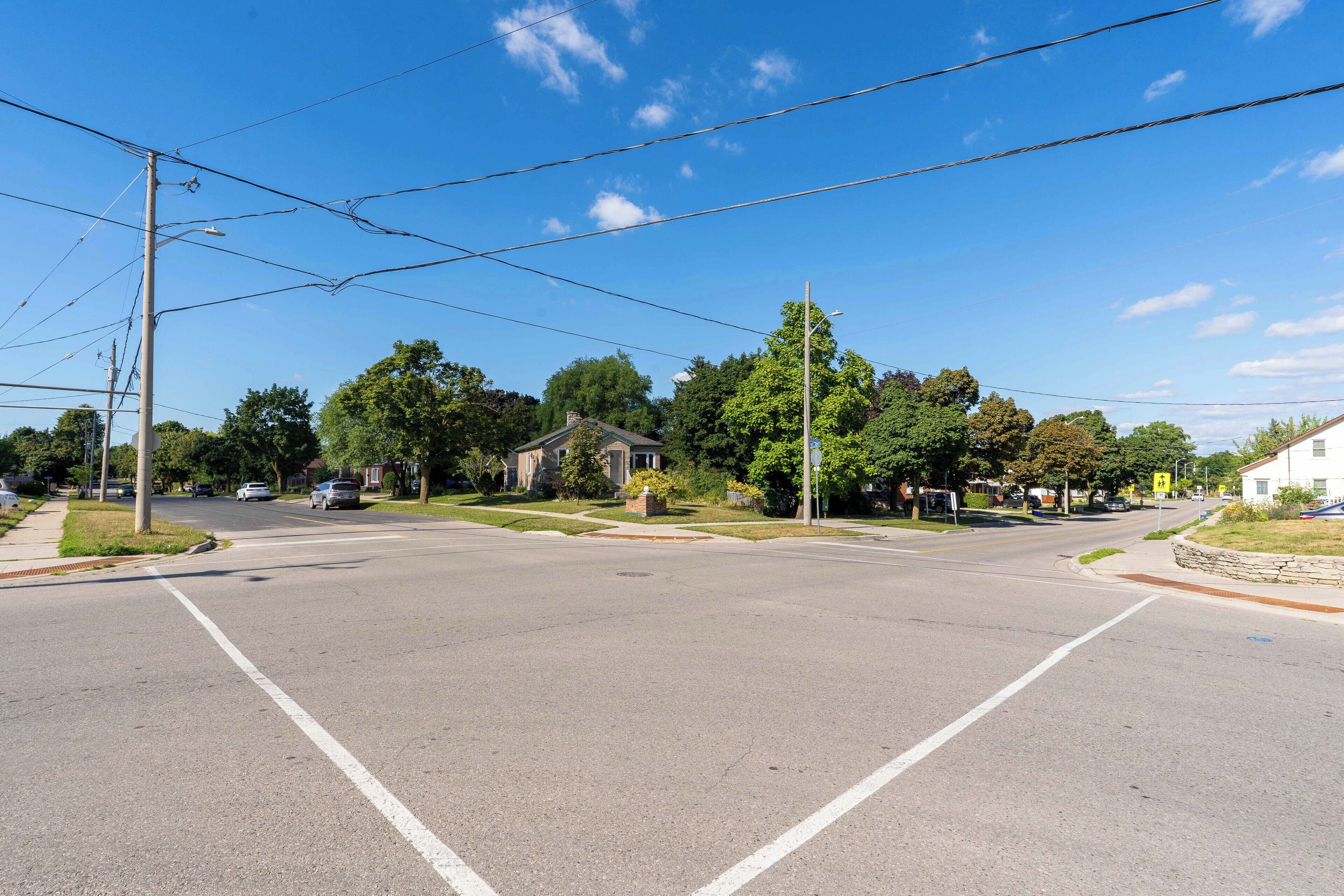 Una intersección suburbana con cielo despejado, casas y postes de servicios públicos.