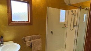 Ein Badezimmer mit Duschkabine aus Glas, Waschbecken, Fenster und einer Kandelaberleuchte.