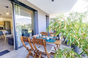 Un espace repas moderne avec une table dressée pour quatre personnes, des chaises en bois, une plante en pot et une vue sur les montagnes par une porte vitrée.