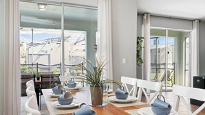 Un coin repas avec une table en bois dressée pour quatre personnes, des chaises blanches et une plante en pot.