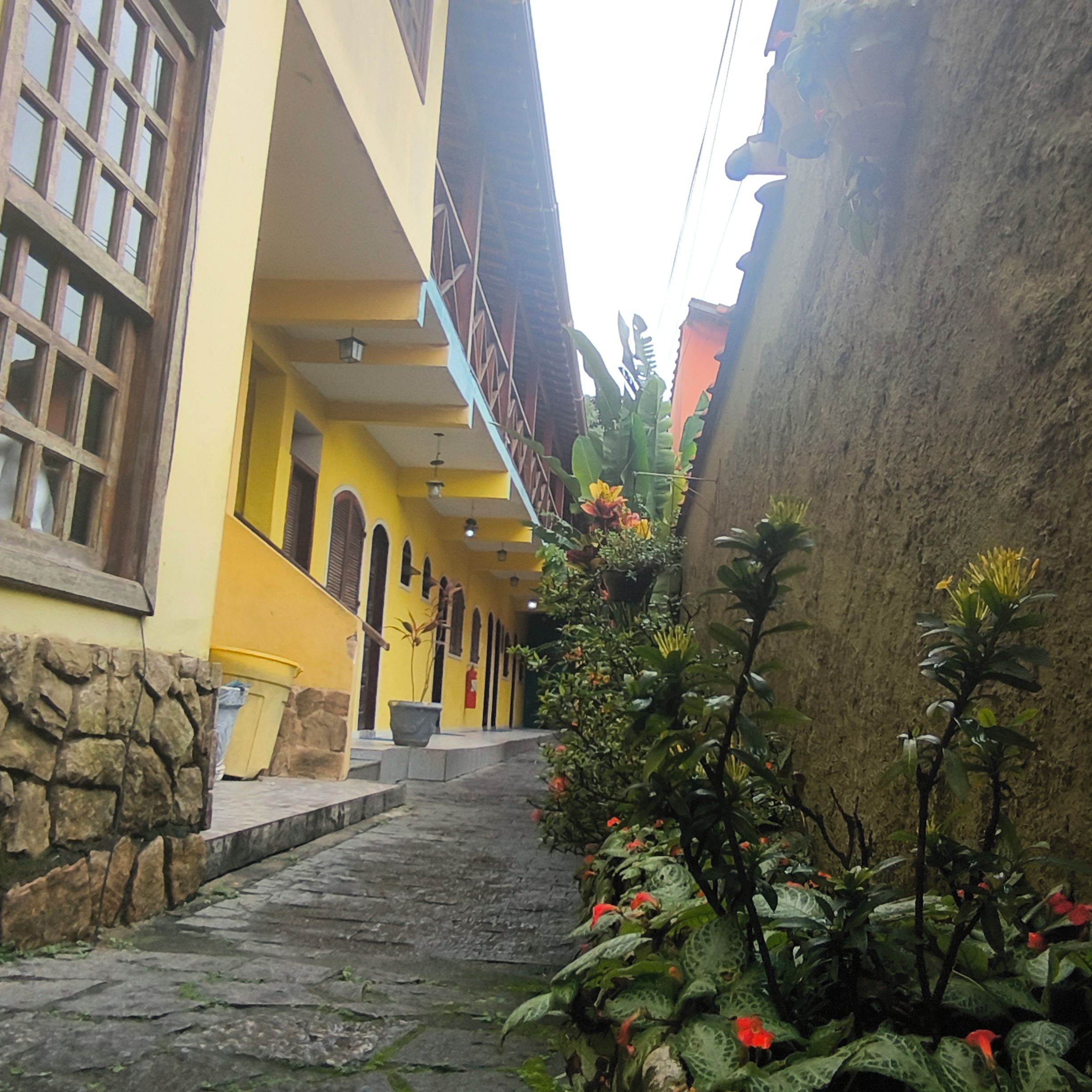 A narrow stone pathway leading to a yellow building with multiple windows and a staircase.