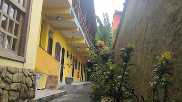 A narrow stone pathway leading to a yellow building with multiple windows and a staircase.