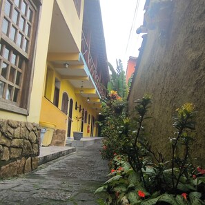Un estrecho sendero de piedra que lleva a un edificio amarillo con varias ventanas y una escalera.